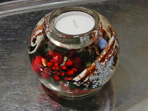 Okrągły świecznik na tealight łączy przezroczyste szkło z czerwonymi i brązowymi akcentami świątecznymi.